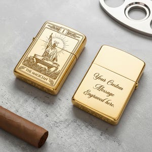 May include: Two gold-colored lighters. One lighter features an engraved image of The Magician tarot card. The other lighter has the text "Your Custom Message Engraved here." A cigar and a metal cigar cutter are also visible.