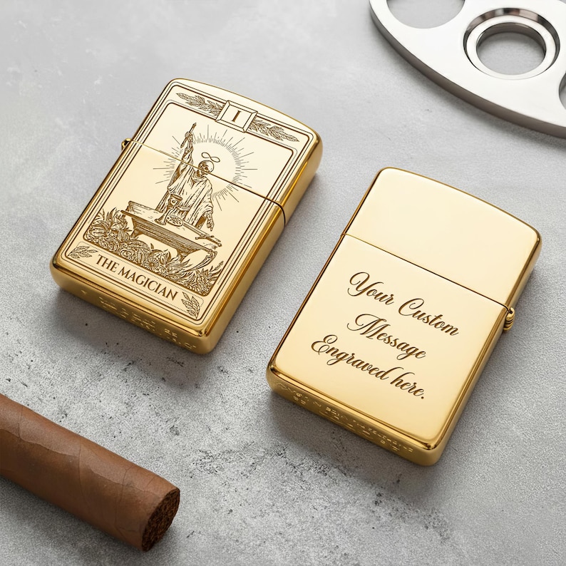 May include: Two gold-colored lighters. One lighter features an engraved image of The Magician tarot card. The other lighter has the text "Your Custom Message Engraved here." A cigar and a metal cigar cutter are also visible.