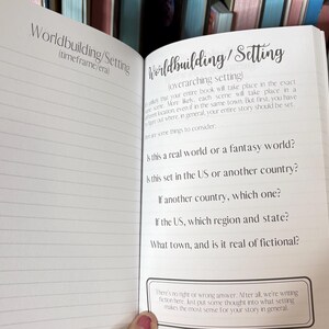 May include: A notebook page with the title "Worldbuilding/Setting" and a list of questions to help writers develop their story's setting. The questions include: "Is this a real world or a fantasy world?", "Is this set in the US or another country?", and "What town, and is it real or fictional?"