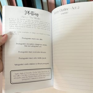 May include: A notebook with a white cover and lined pages. The notebook is open to a page with the title "Plotting (Act 2 - The Middle)" and a list of plot points for the middle act of a story. The next page is titled "Story Outline - Act 2 (middle)" and has lined pages for writing.