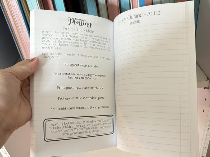 May include: A notebook with a white cover and lined pages. The notebook is open to a page with the title "Plotting (Act 2 - The Middle)" and a list of plot points for the middle act of a story. The next page is titled "Story Outline - Act 2 (middle)" and has lined pages for writing.