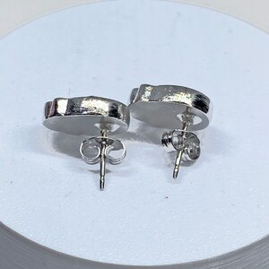 May include: A pair of silver stud earrings with a unique, abstract shape. The earrings have a post and butterfly backing.
