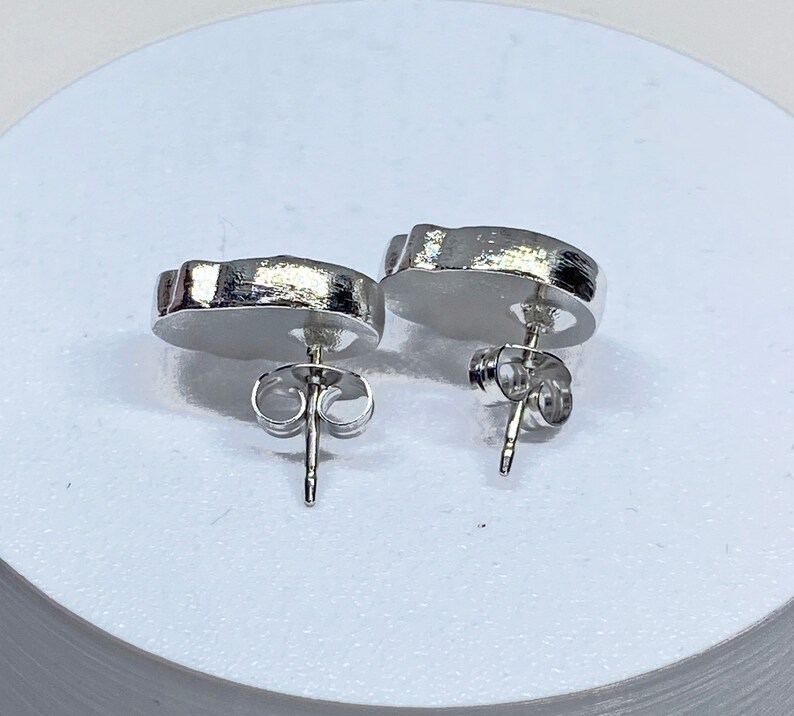 May include: A pair of silver stud earrings with a unique, abstract shape. The earrings have a post and butterfly backing.