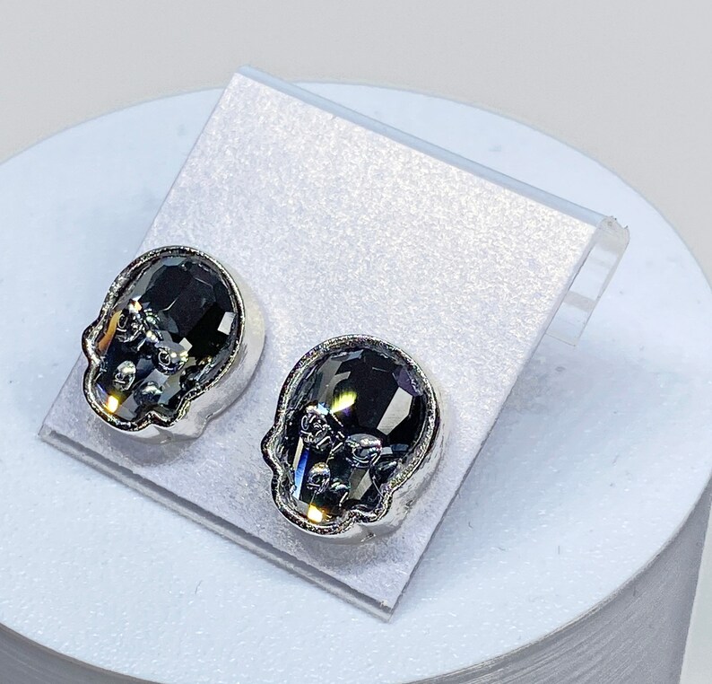 May include: A pair of silver skull stud earrings with black crystal accents.