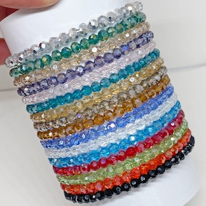 May include: A stack of 15 crystal bracelets in various colors, including black, red, green, blue, and clear. The bracelets are made of small, faceted beads.