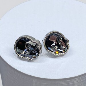 May include: A pair of silver skull-shaped earrings with black crystal accents.