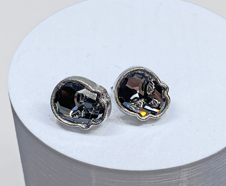 May include: A pair of silver skull-shaped earrings with black crystal accents.