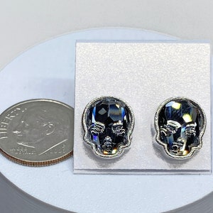 May include: A pair of silver skull stud earrings with black crystal accents. The earrings are displayed on a white background.