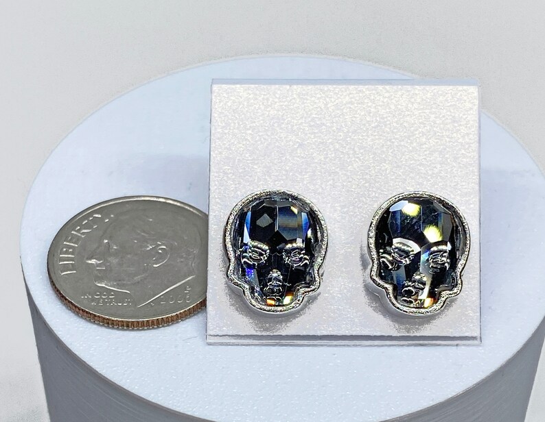 May include: A pair of silver skull stud earrings with black crystal accents. The earrings are displayed on a white background.