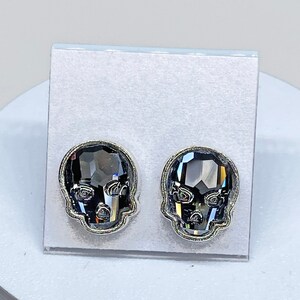 May include: A pair of silver skull stud earrings with black crystal accents.