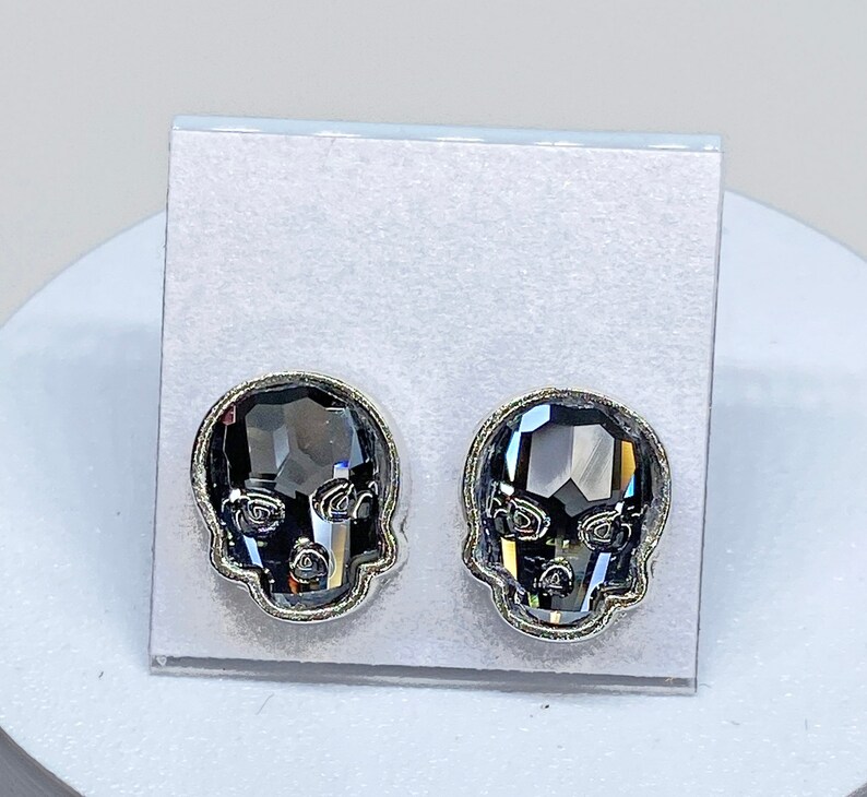 May include: A pair of silver skull stud earrings with black crystal accents.