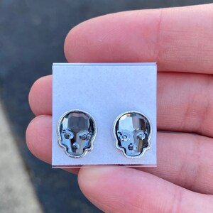 May include: A pair of silver skull stud earrings with clear crystal accents.