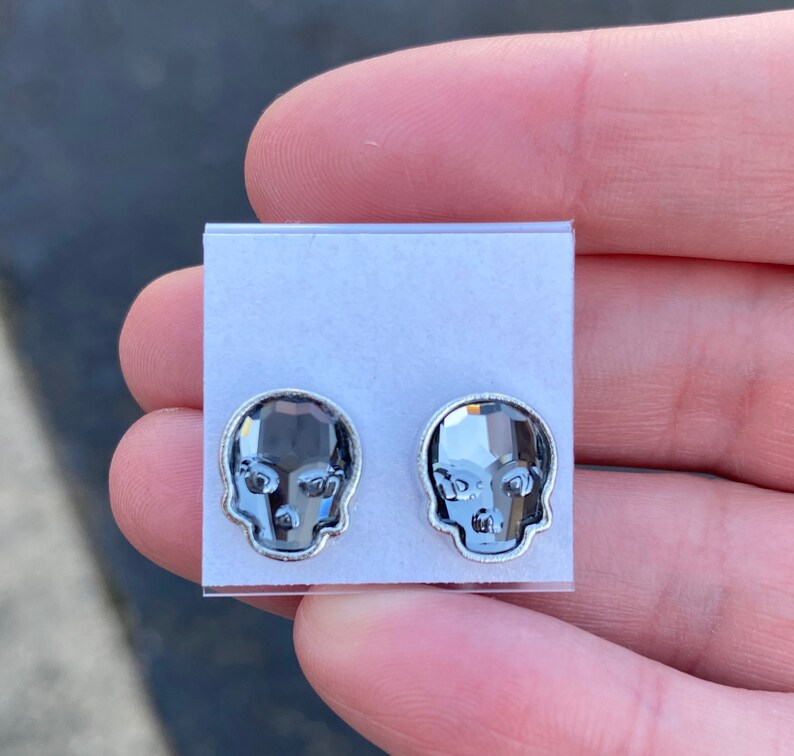 May include: A pair of silver skull stud earrings with clear crystal accents.