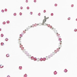 May include: A delicate pink and clear crystal bracelet with a silver ribbon charm. The bracelet is made with small, faceted beads and is perfect for adding a touch of sparkle to any outfit.