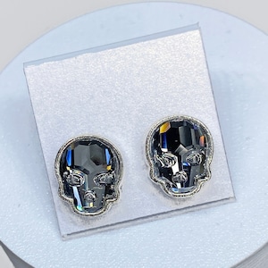 May include: A pair of silver skull stud earrings with black crystal accents.