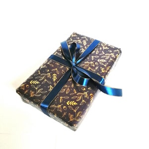 May include: A gift box wrapped in dark brown paper with a gold leaf pattern and tied with a blue ribbon.