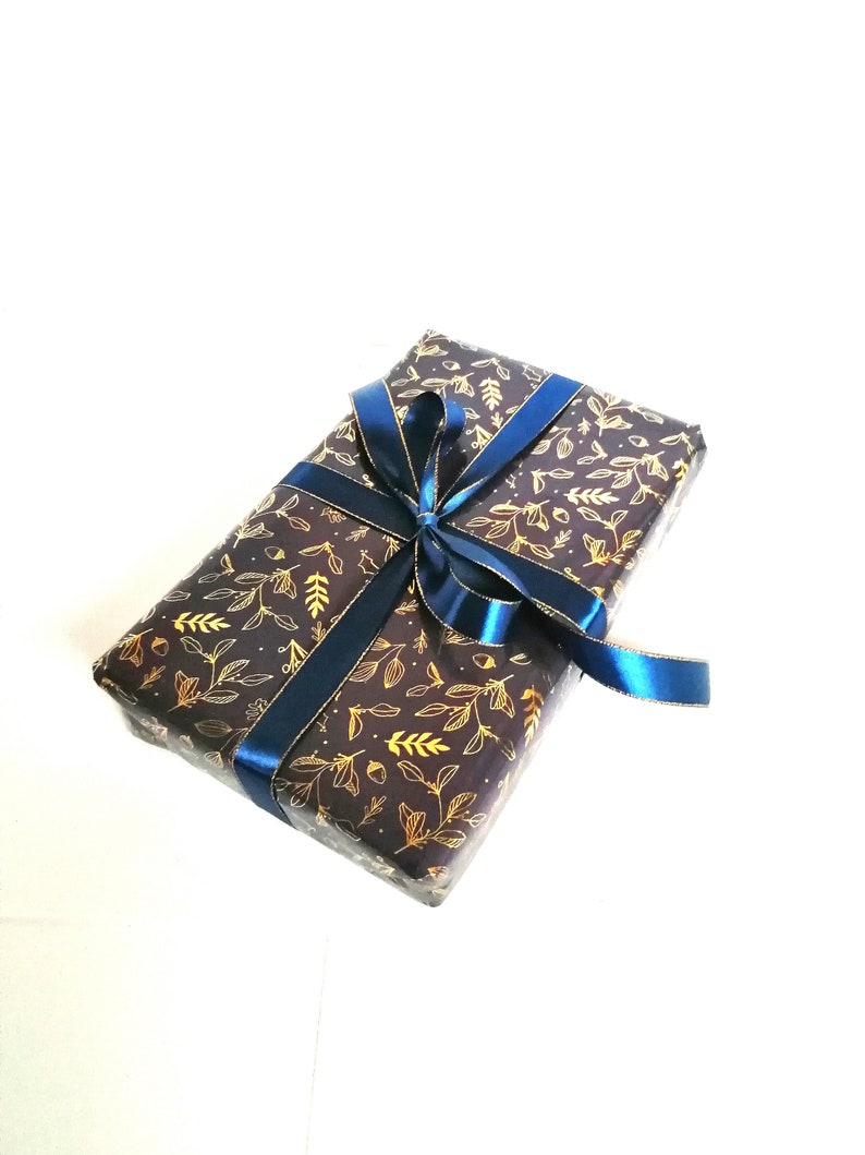 May include: A gift box wrapped in dark brown paper with a gold leaf pattern and tied with a blue ribbon.