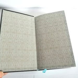 May include: An open notebook with a black cover and a patterned paper interior. The notebook is open to a blank page.