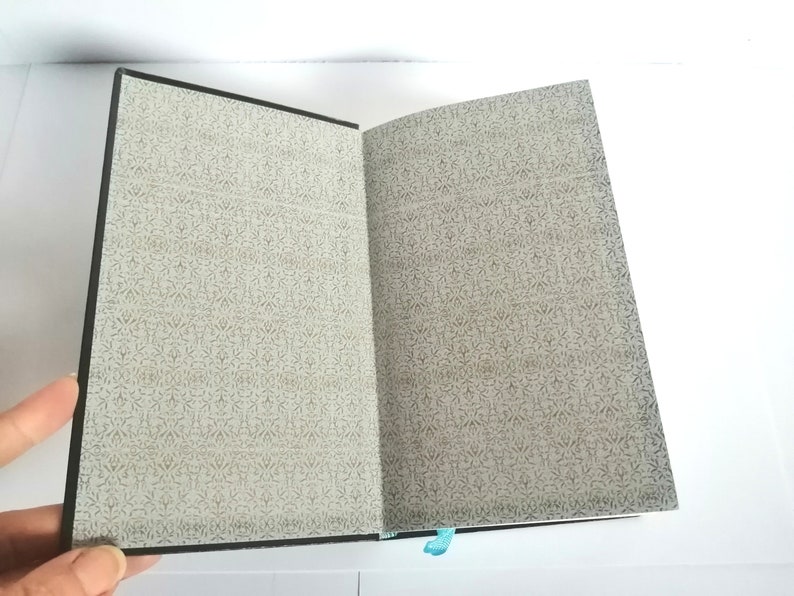 May include: An open notebook with a black cover and a patterned paper interior. The notebook is open to a blank page.