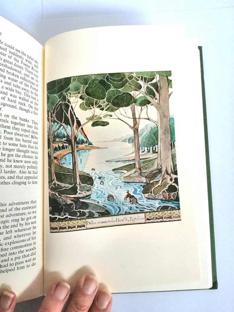 K&ouml;nnte beinhalten: Eine Illustration eines Hobbits, Bilbo Beutlin, der mit einem Boot einen Fluss hinunterf&auml;hrt. Der Fluss ist von B&auml;umen umgeben und der Himmel ist blassblau. Der Text "Bilbo kommt zu den H&uuml;tten der Ruhe-Elfen" befindet sich am unteren Rand des Bildes.