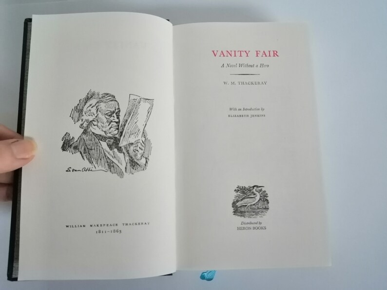 May include: A black and white illustration of a man reading a newspaper. The text on the cover reads "Vanity Fair: A Novel Without a Hero" by W. M. Thackeray. The book is published by Heron Books.