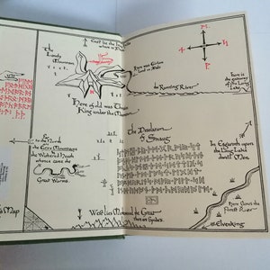K&ouml;nnte beinhalten: Eine Schwarzwei&szlig;karte eines fiktiven Landes mit dem Text "Thror's Map" in der linken unteren Ecke. Die Karte zeigt eine Bergkette, einen Fluss und einen See. Der Text "Here of old was Thorin King under the Mountain" ist in roter Tinte geschrieben.