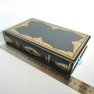 May include: A black leather-bound book with gold-colored decorative accents and the title "Vanity Fair" by W.M. Thackeray on the spine.