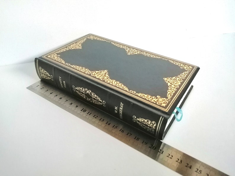 May include: A black leather-bound book with gold-colored decorative accents and the title "Vanity Fair" by W.M. Thackeray on the spine.