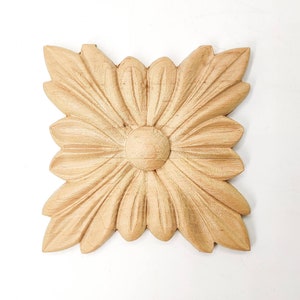 May include: A wooden carved flower design with a raised center, in a light brown color.