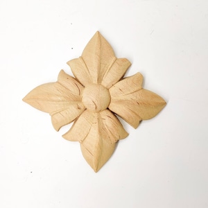 May include: A wooden decorative accent piece in the shape of a flower with a center circle. The piece is light brown and has a natural wood finish.