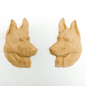 May include: Two wooden dog head sculptures, each with a detailed carving of a dog's face. The sculptures are facing each other, with their noses almost touching.