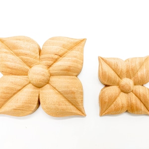May include: Two wooden flower-shaped embellishments. The larger one is about 4 inches wide and the smaller one is about 2 inches wide. Both are carved with a detailed floral design.