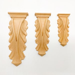 May include: Three wooden corbels with a leaf design. The corbels are different sizes and are arranged in a row from largest to smallest.