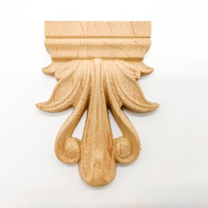 Puede incluir: Una pieza de acento decorativa de madera con un diseño floral tallado. La pieza es sin terminar y tiene un color de madera natural.