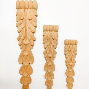 May include: Three wooden decorative pieces with a carved leaf design. The pieces are different sizes and are arranged in a row from largest to smallest.