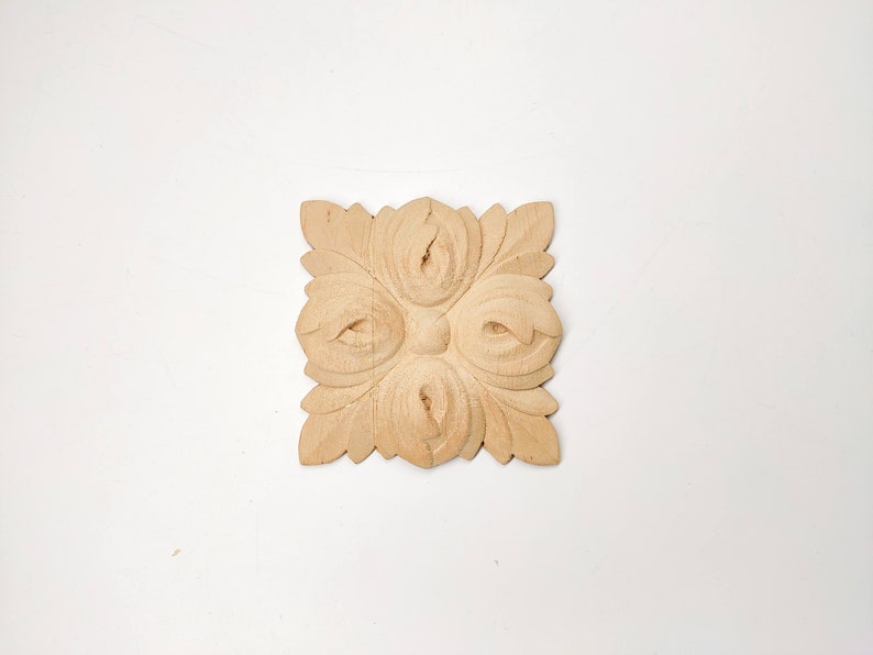 Puede incluir: Un adorno cuadrado de madera tallada con un dise&ntilde;o floral. El adorno es de color marr&oacute;n claro y tiene un dise&ntilde;o en relieve.