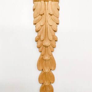 May include: A wooden carved ornament with a leaf design. The ornament is light brown in color and has a detailed, intricate design.