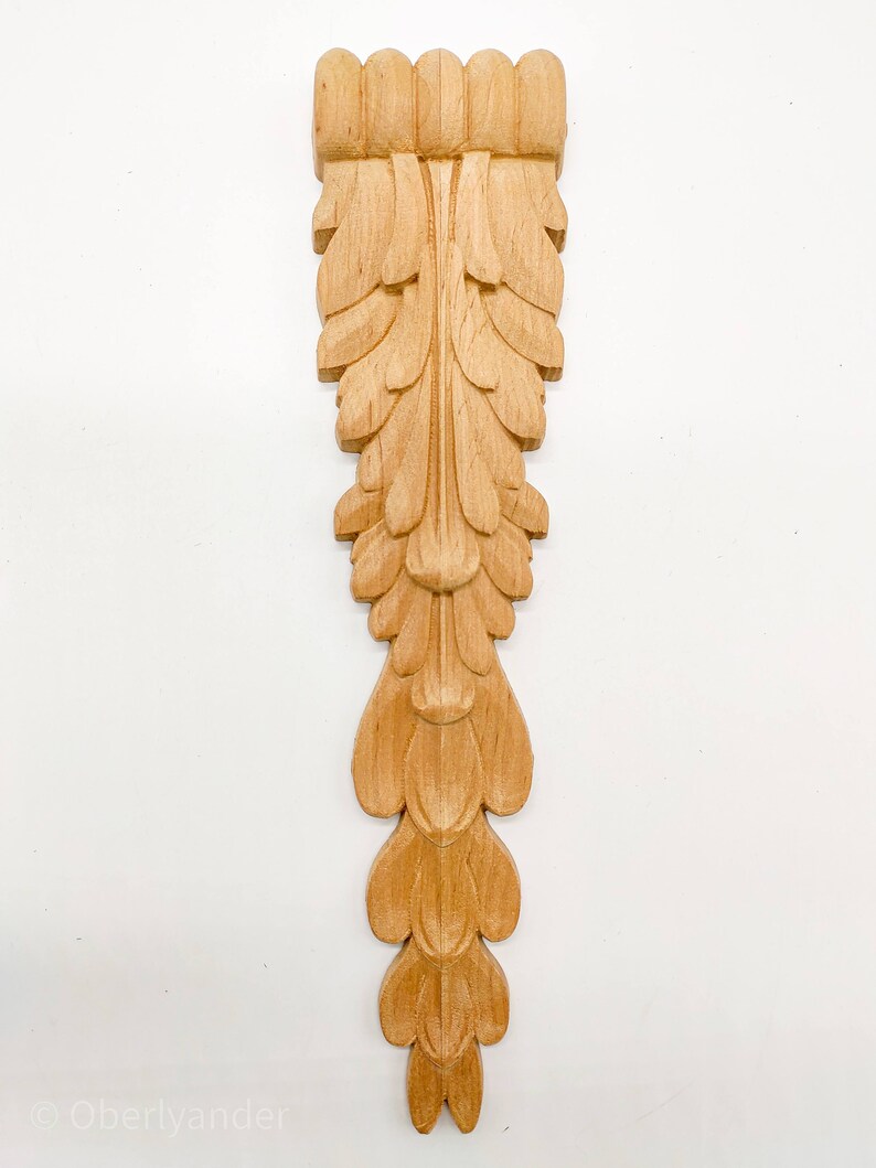 May include: A wooden carved ornament with a leaf design. The ornament is light brown in color and has a detailed, intricate design.