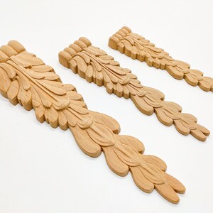 May include: Three wooden decorative pieces with a carved leaf design. The pieces are different sizes and are arranged in a row from largest to smallest.