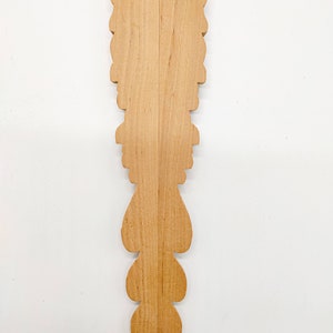 May include: A wooden decorative piece with a carved design. The piece is made of light brown wood and has a symmetrical design with a series of teardrop shapes.
