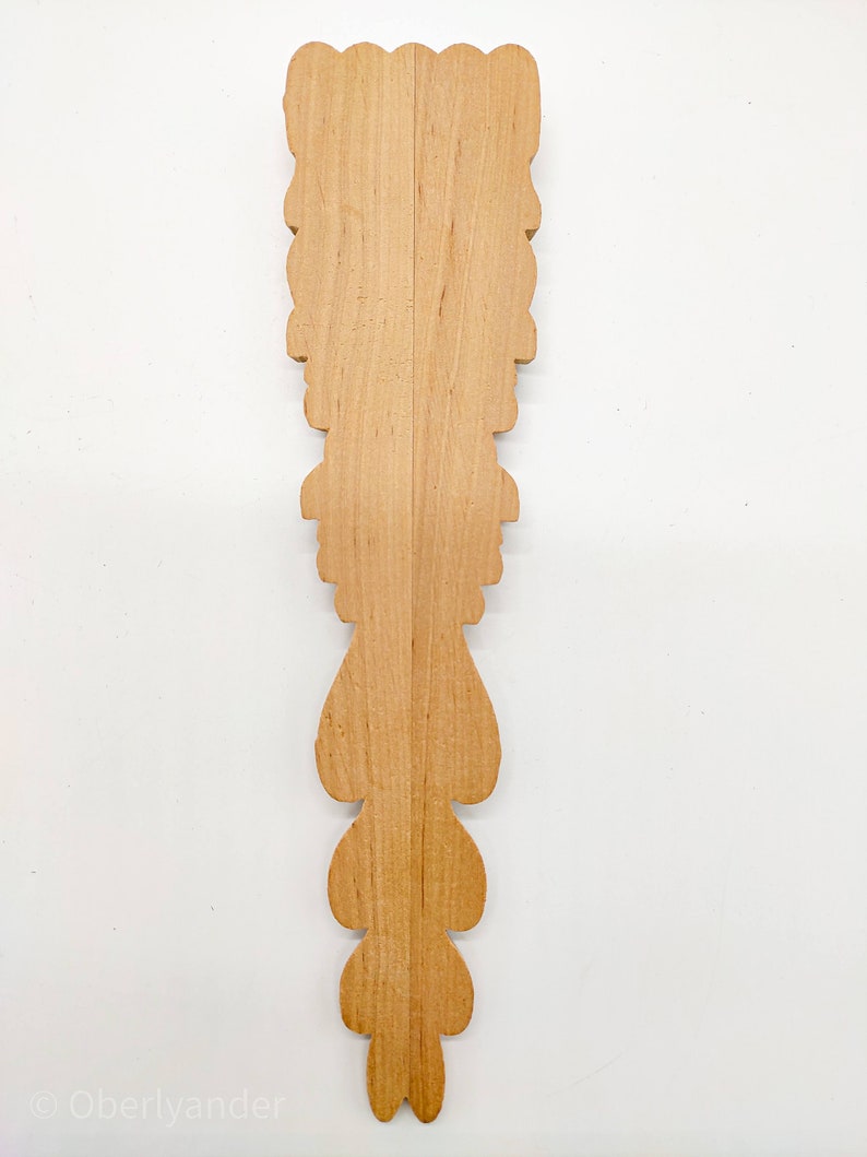 May include: A wooden decorative piece with a carved design. The piece is made of light brown wood and has a symmetrical design with a series of teardrop shapes.
