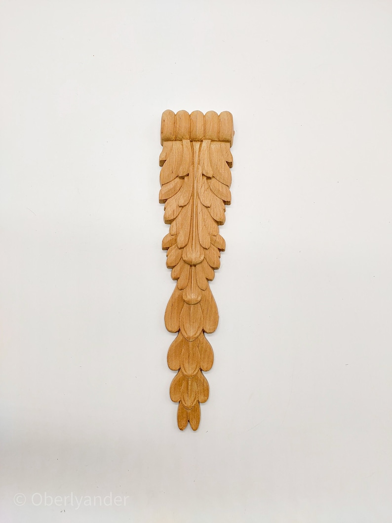 May include: A wooden carved ornament with a leaf design. The ornament is light brown and has a detailed, intricate design.