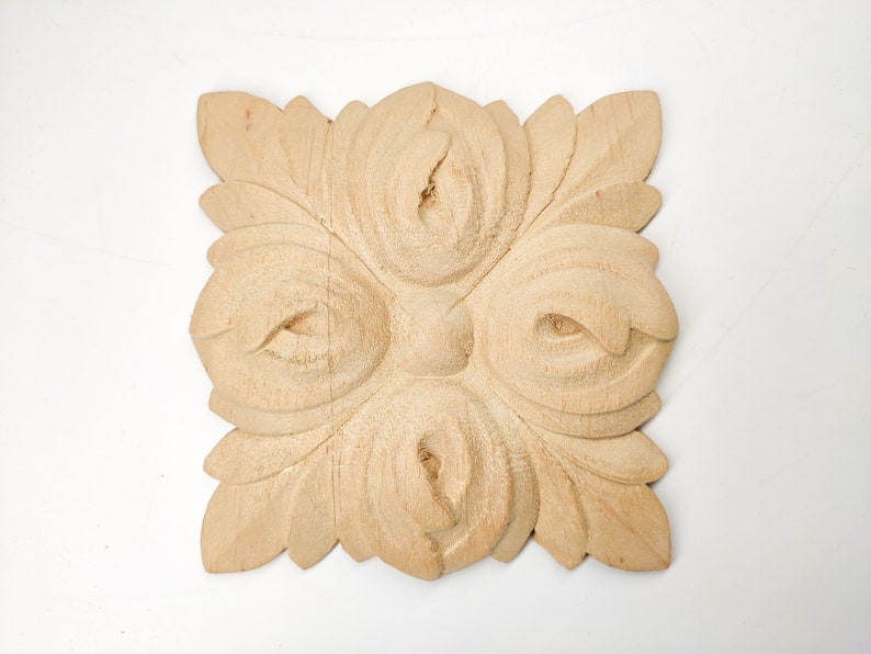 Puede incluir: Un adorno de madera tallado con un dise&ntilde;o floral. El adorno es de color marr&oacute;n claro y tiene una forma cuadrada.