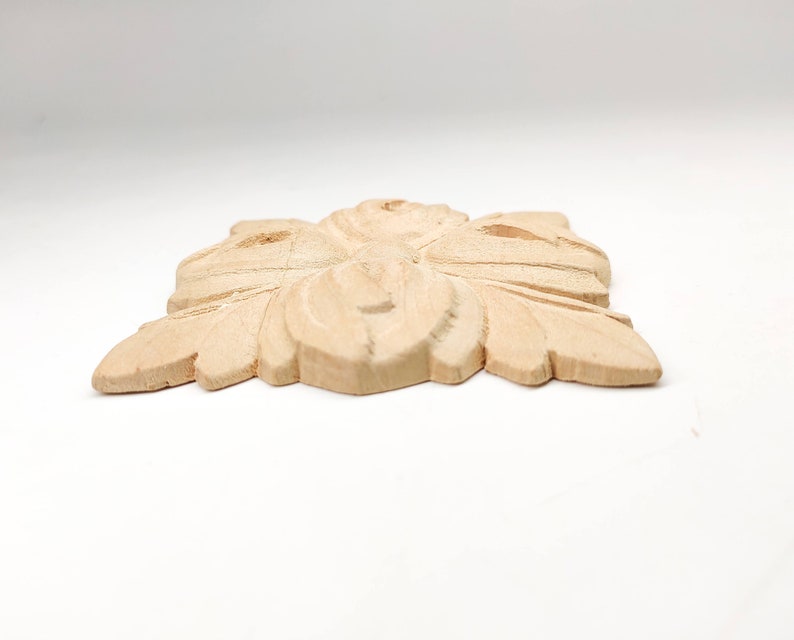 Puede incluir: Un adorno decorativo de madera marr&oacute;n claro con un dise&ntilde;o floral tallado. El adorno tiene forma de cuadrado con esquinas redondeadas.