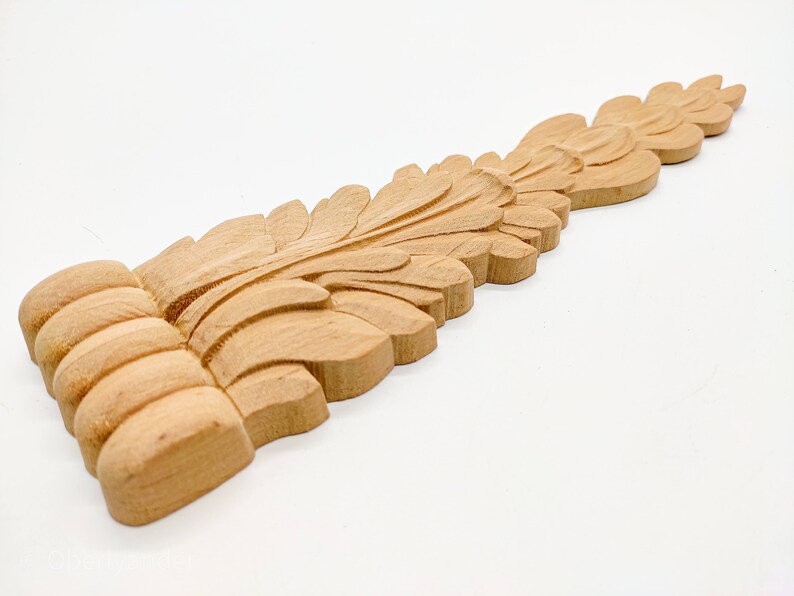 May include: A wooden carved leaf design with a detailed, intricate pattern. The design is light brown in color and has a smooth, polished finish.