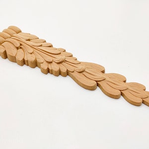 May include: A carved wooden decorative piece with a leaf design. The piece is light brown in color and has a long, narrow shape.