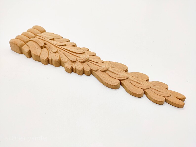 May include: A carved wooden decorative piece with a leaf design. The piece is light brown in color and has a long, narrow shape.