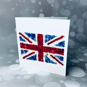 May include: A white card with a Union Jack flag made of buttons. The flag is made of red, white, and blue buttons.