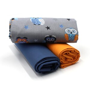 May include: Three fabric rolls, one with a grey background and a pattern of owls and stars, one blue, and one orange.