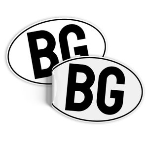 Może przedstawiać: Dwie białe owalne naklejki z literami "BG" w pogrubionej czarnej czcionce. Jedna naklejka jest częściowo odklejona, odsłaniając klej. Naklejki są prawdopodobnie przeznaczone do pojazdu, na białym tle.